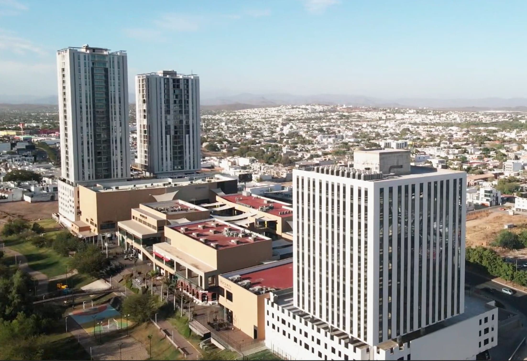 Vista aérea del Corporativo Cuatro Ríos: la torre de oficinas blanca junto al centro comercial y las torres residenciales, con Culiacán al fondo